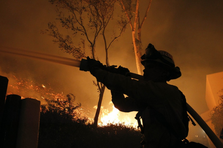 Firefighter Cole Bellatti hoses a hillside behind stores in the River Village shopping center at Highway 76 and South Mission Road as the Lilac Fire burns through Bonsall in 2017.  (Hayne Palmour IV/San Diego Union-Tribune)